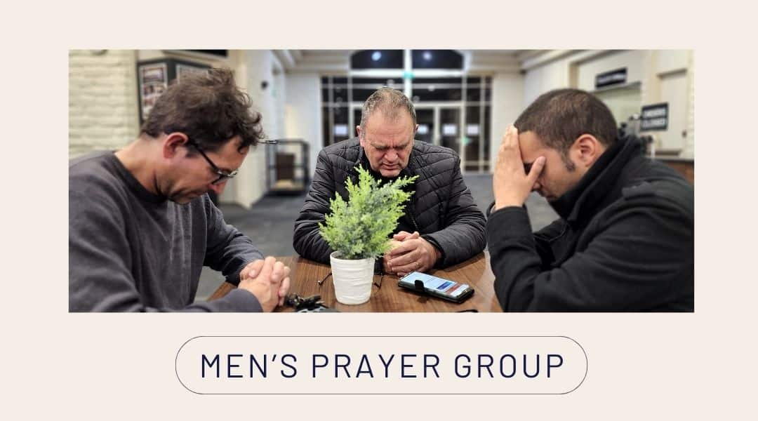 Image of three men praying around a table. Men's Prayer Group.