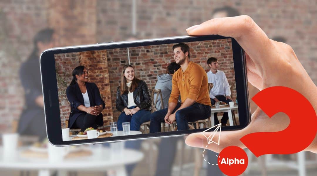 Image of a hand holding a mobile. The photo on the mobile is three happy young adults doing the Alpha Course. Large ? Alpha displayed on the banner.