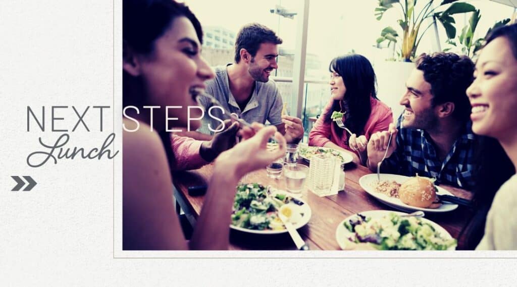 Photo of young adults having lunch on a timber table looking happy during the day. Next Steps Lunch.