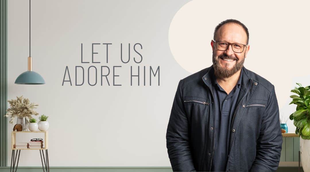 Image of Pastor Braam wearing a black jacket and glasses smiling. There is a side table behind him with fake plants on it.