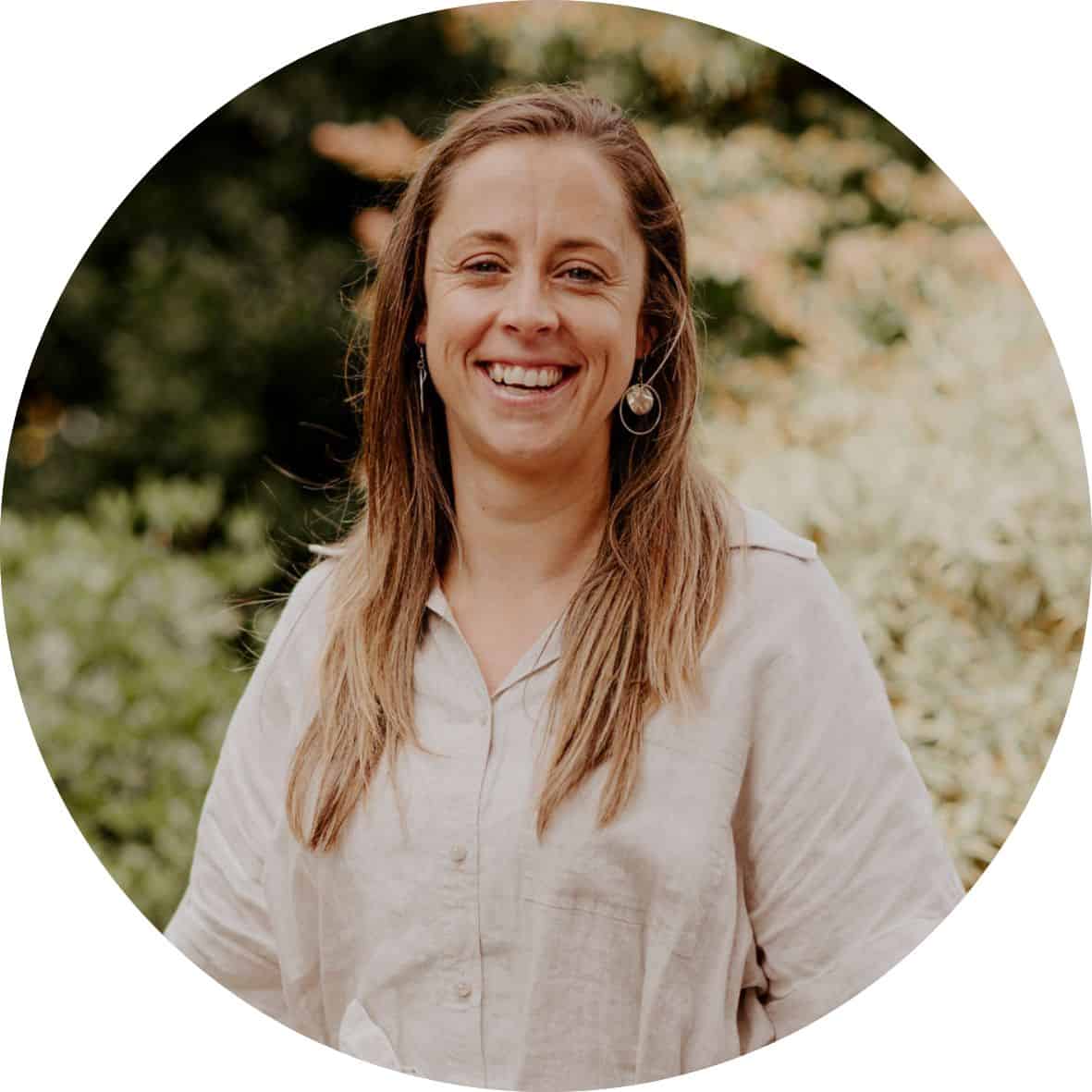 Alex Cuss is wearing a beige dress standing in front of trees