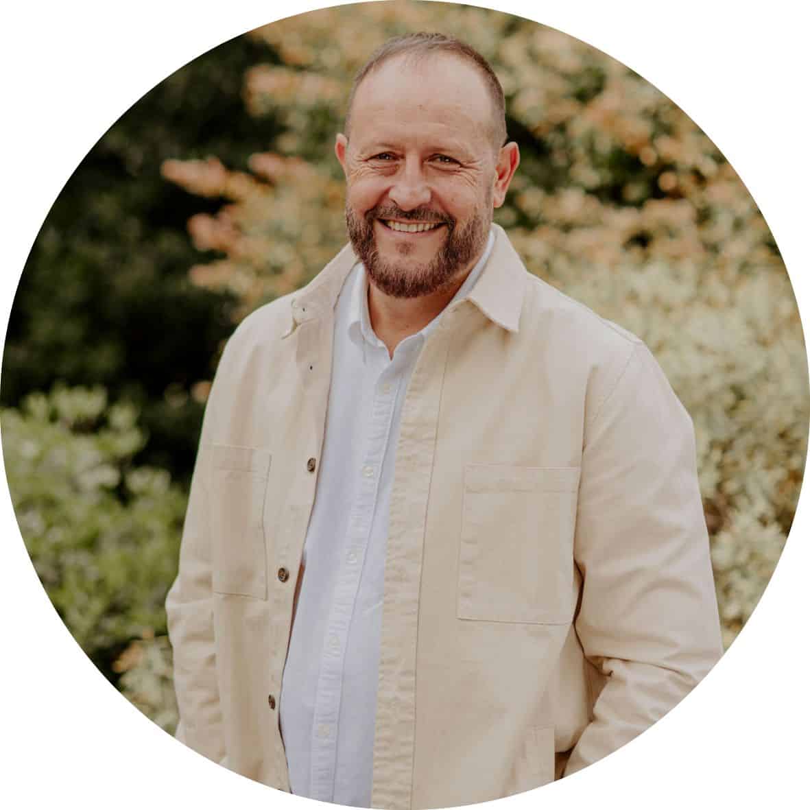 Pastor Braam Botha is wearing a white shirt with beige jacket in front of trees
