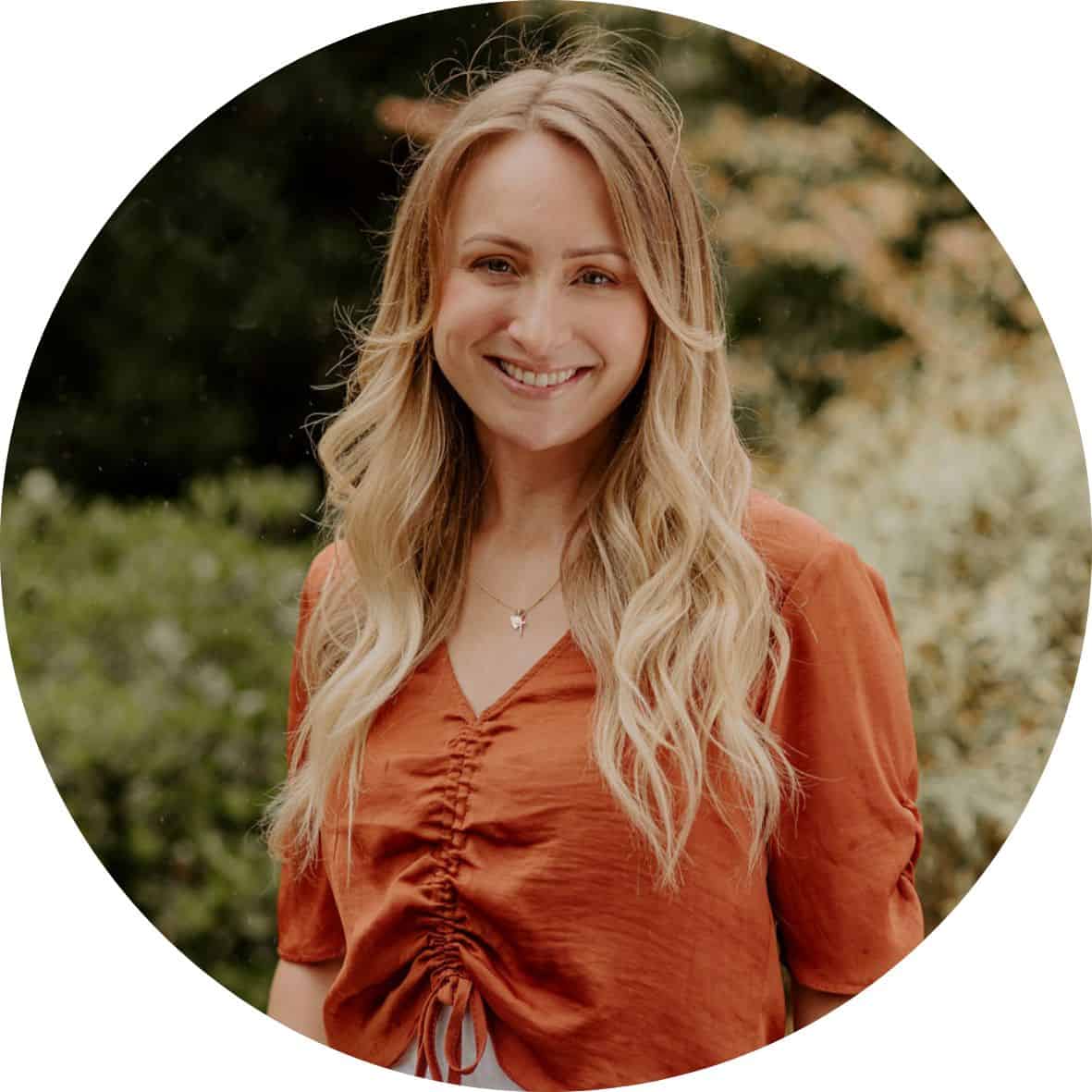 Jaclyn Szabo is wearing a burnt orange shirt standing in front of trees