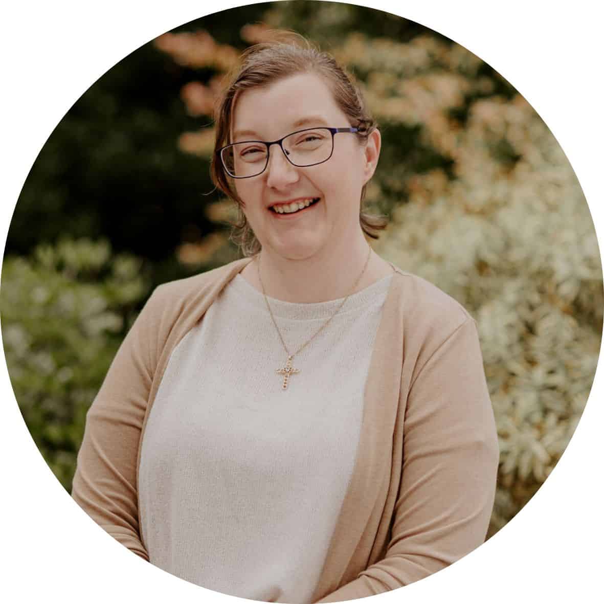 Marry Anne Sidebottom is wearing a white tshirt and tan cardigan and standing in front of trees