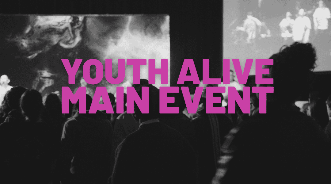 Image of youth in a dark arena looking at the stage worshipping.