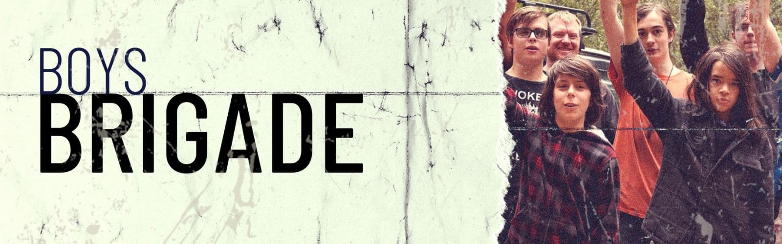 Image of a group of boys wearing old flannels and tracsuites outdoors in the bush holding their arms in the air